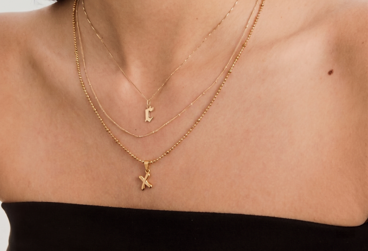 Gold-tone initial pendant necklace on a warm white background